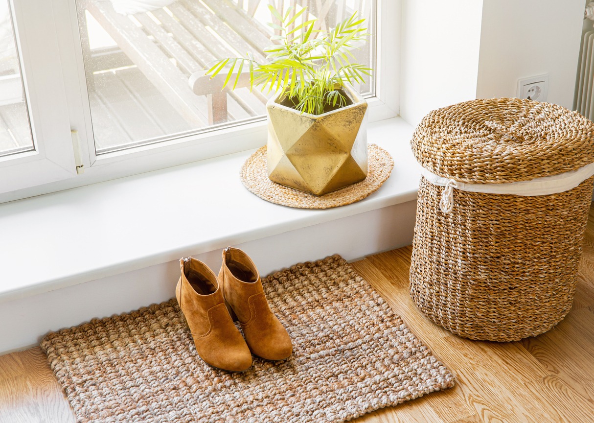 A room with a jute doormat, golden plant pot, and seagrass laundry basket