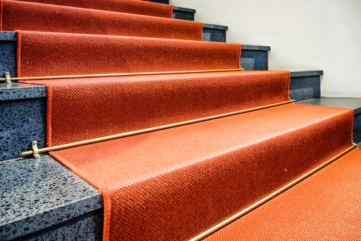 A marble staircase with red carpet runner and gold rods