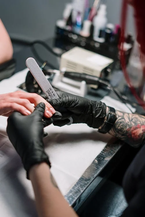 a hand wearing black gloves with a nail file, and a hand of a client