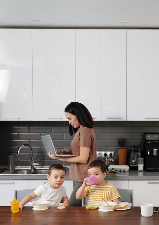 a woman working on her laptop while standing near her Kids eating breakfast