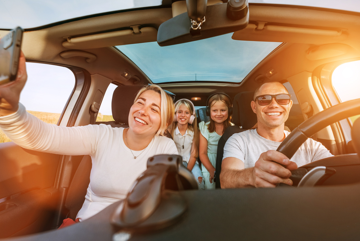 Happy young couple with two daughters inside car during road trip