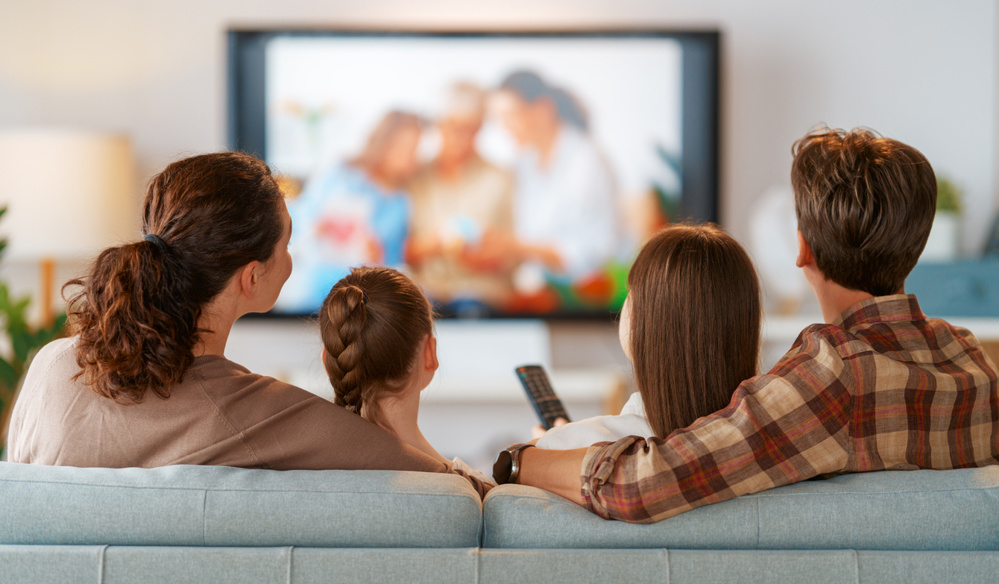 Happy family spending time together. Mother, father and children watching TV, movies with popcorn in the evening at home