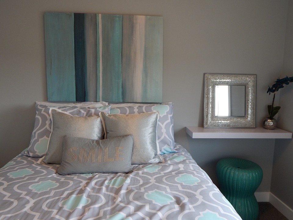 A small bedroom with a gray, teal and white color scheme accented with a teal wicker chair
