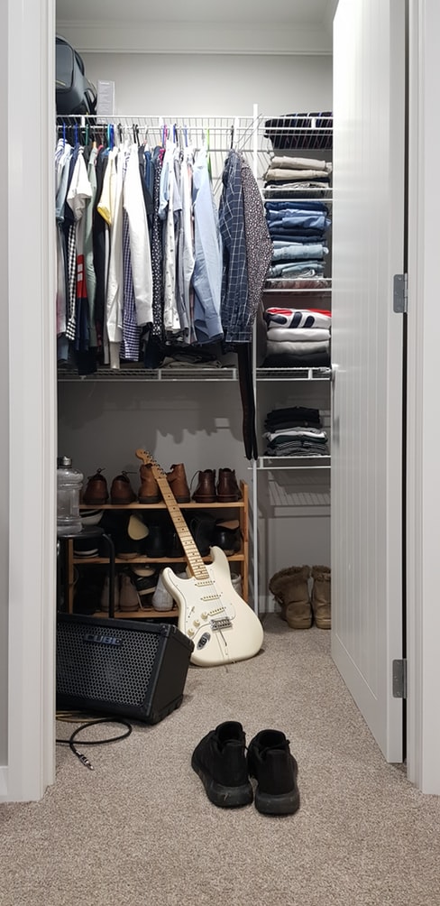 a closet with clothes, shoes, and a guitar