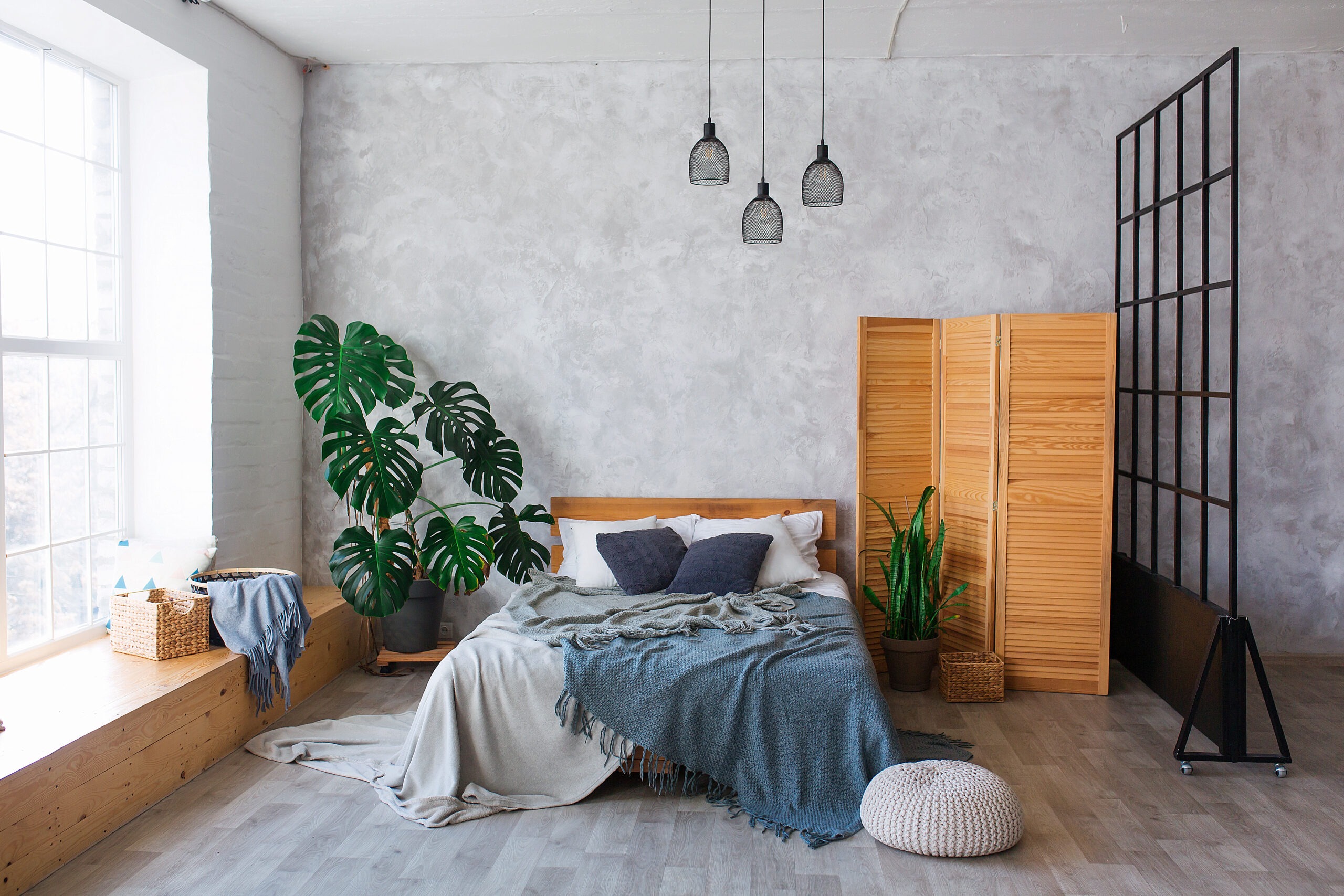 Cozy bedroom area at luxury studio apartment with a free layout in a loft style with big panoramic window and green plant.