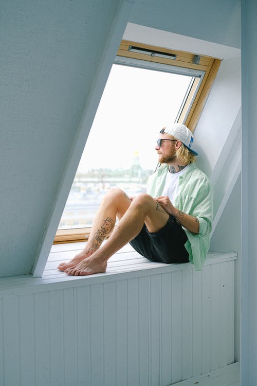 A man sitting on the windowsill in the attic. 