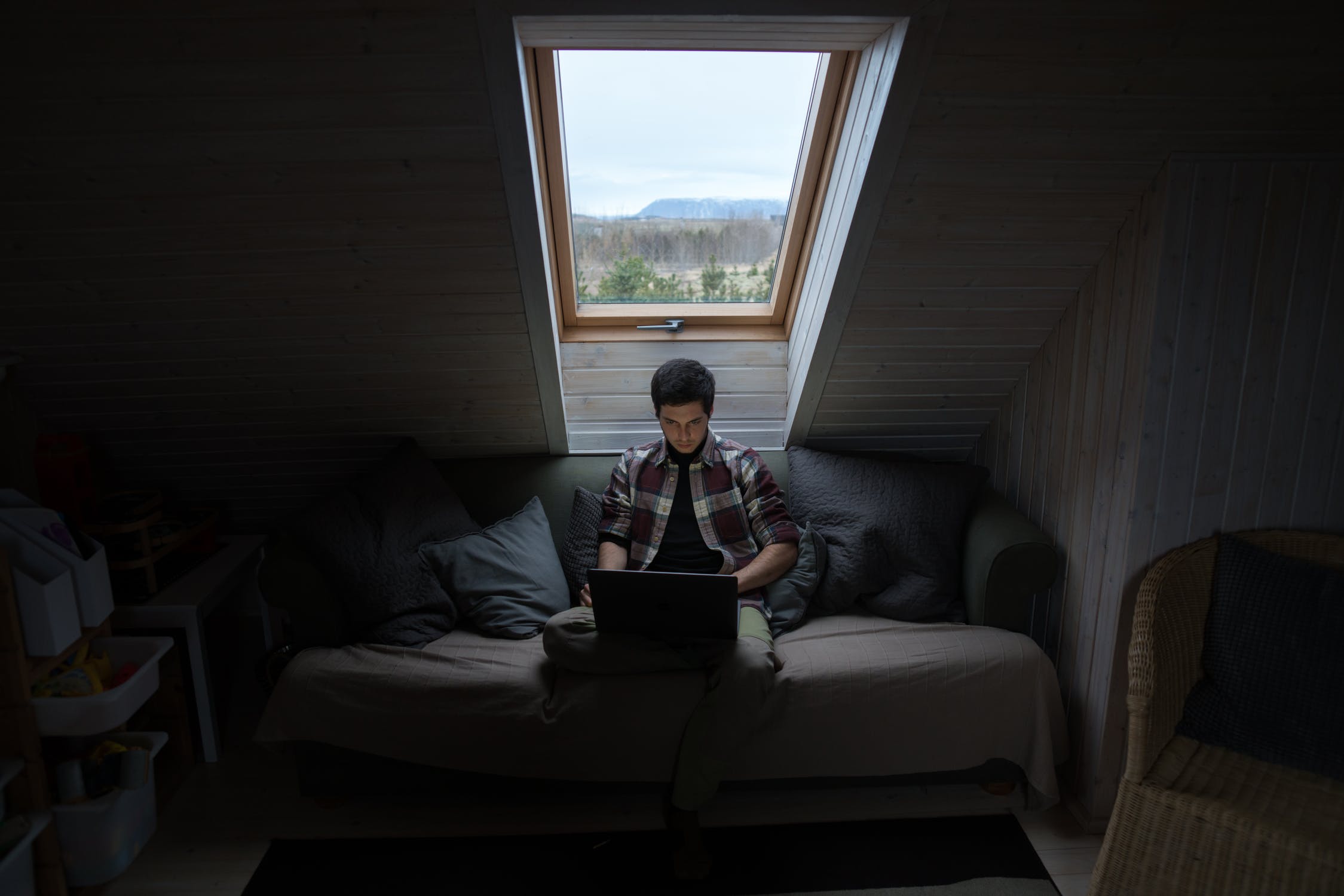 A man using a laptop near his window. 