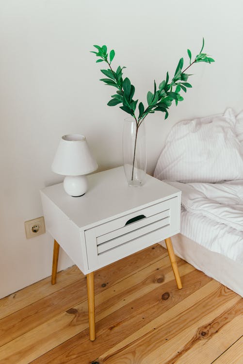 Side table with a lamp and plant beside a bed 
