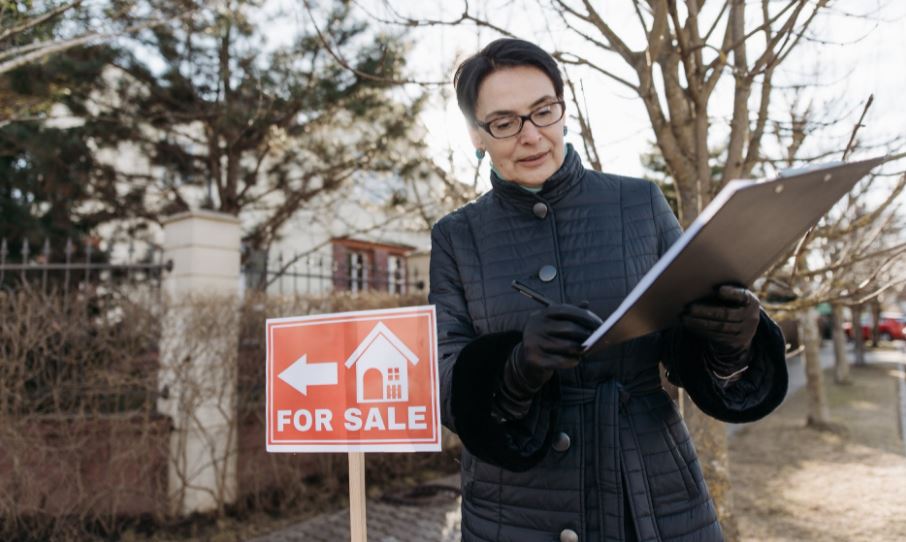 woman beside a house for sale sign