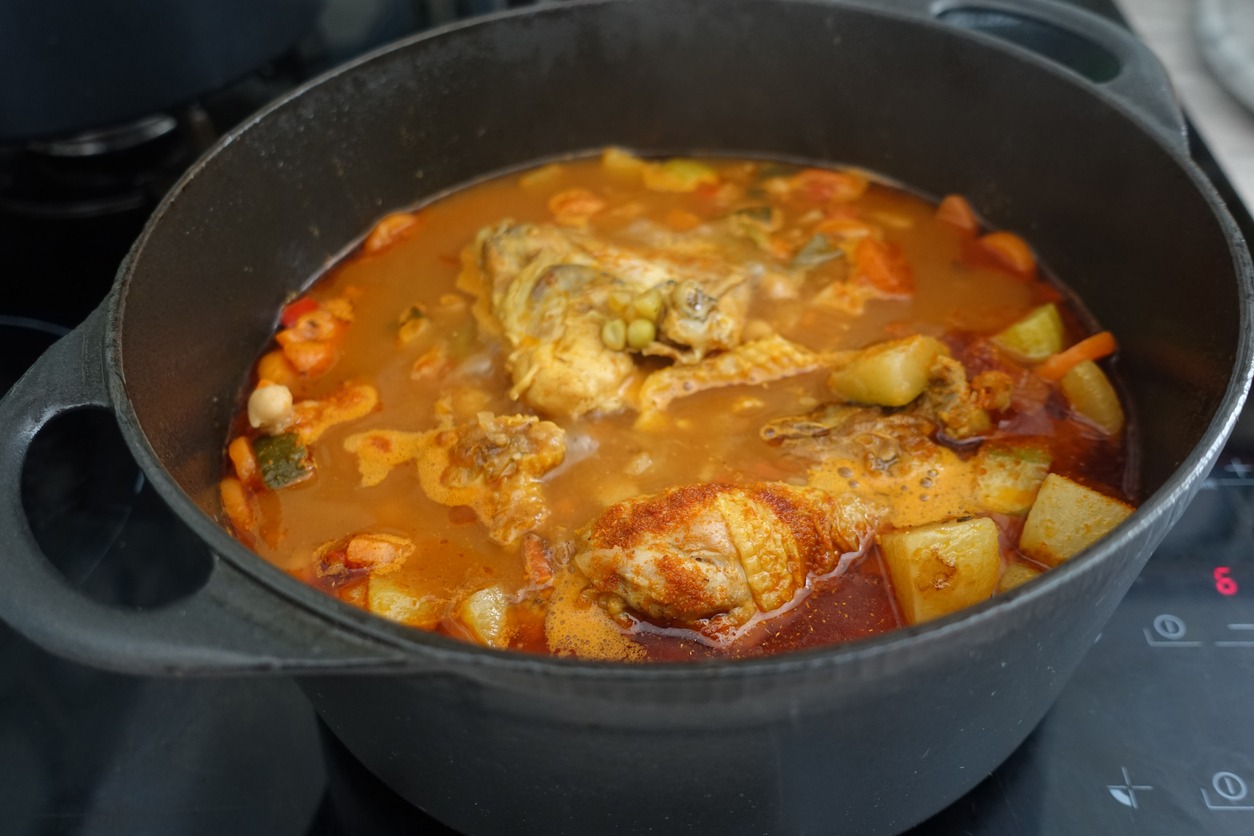Chicken thighs being cooked in a spicy broth with various vegetables Mediterranean cuisine