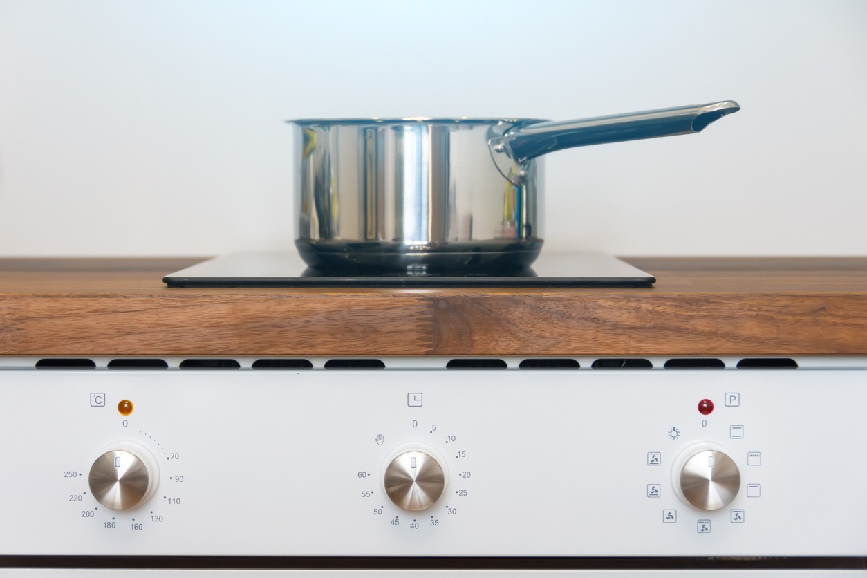 Pot ladle on induction cooker built into wood kitchen worktop view of oven knob relay.