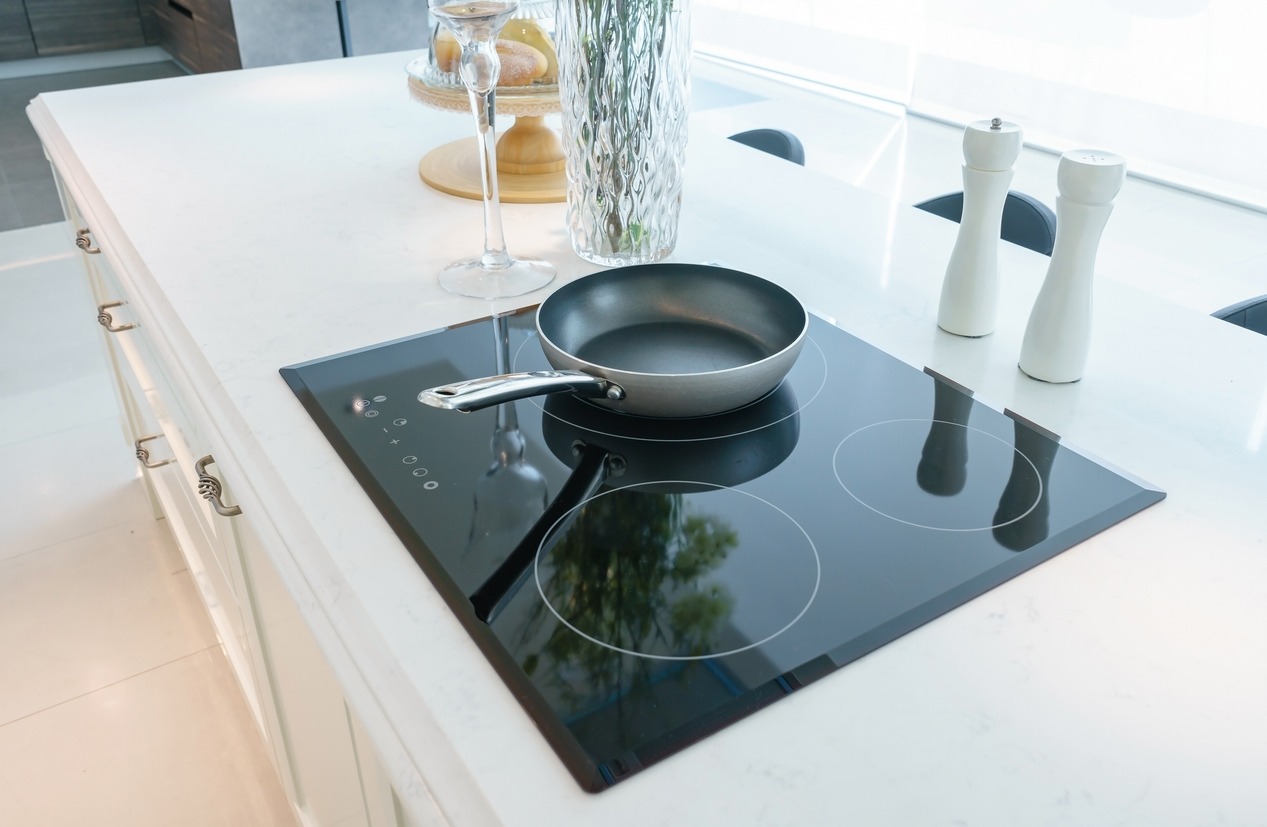 Frying pan on modern black induction stove, cooker, hob or built in cooktop with ceramic top in white kitchen interior