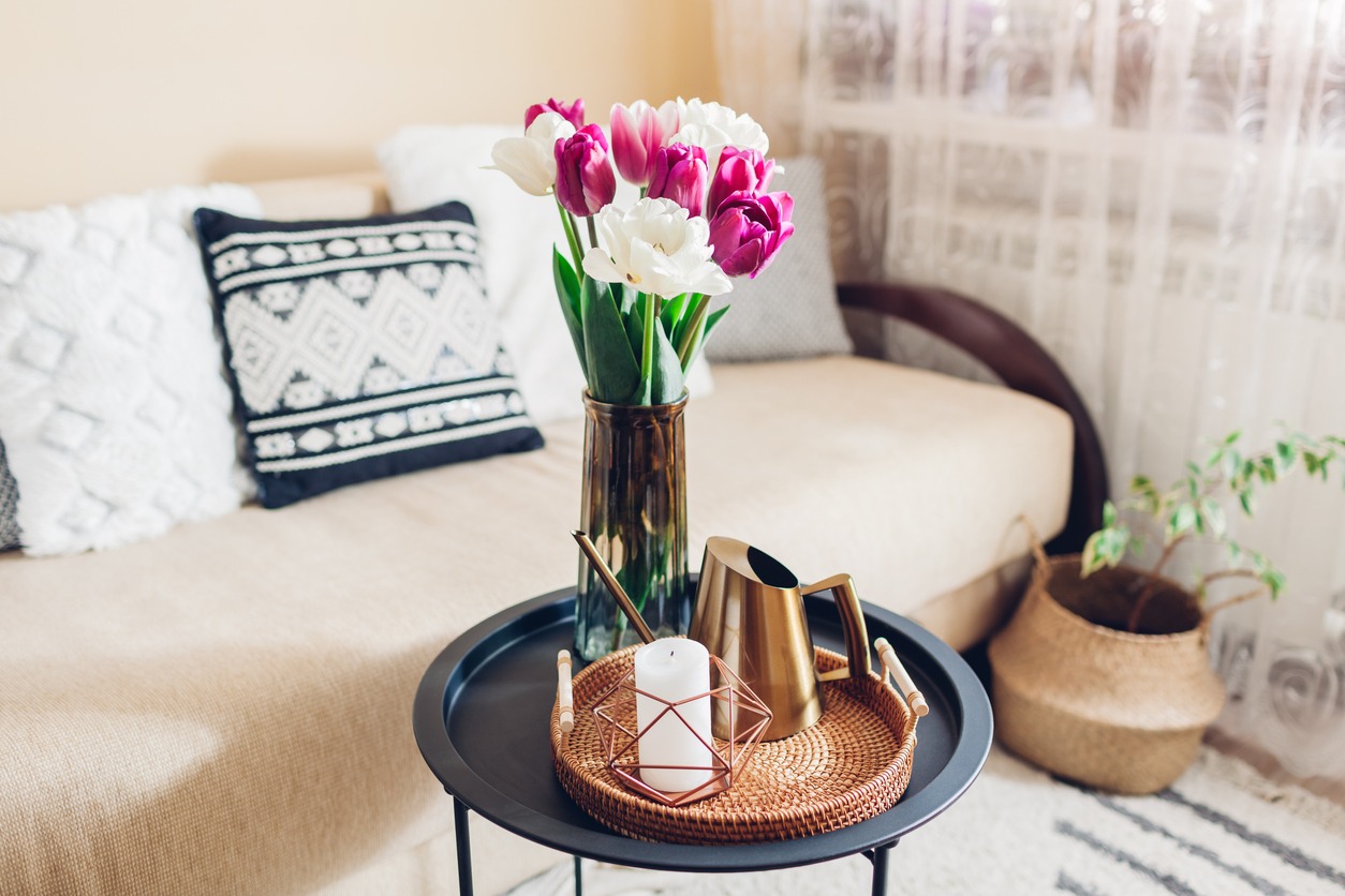 Fresh tulips flowers put in vases on coffee table with candle and watering can on rattan tray
