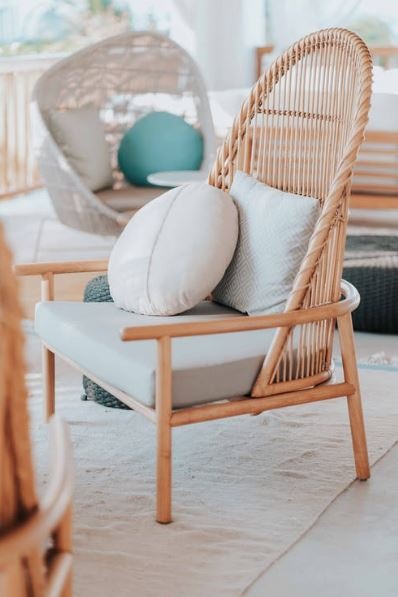 a wicker chair with pillows and a cushion placed oudoors