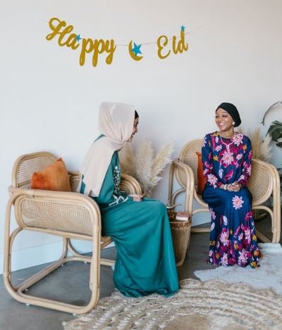 women wearing a hijab sitting on rattan chairs with a “Happy Eid” banner on the white wall