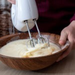 person using an electric hand mixer to mix dough