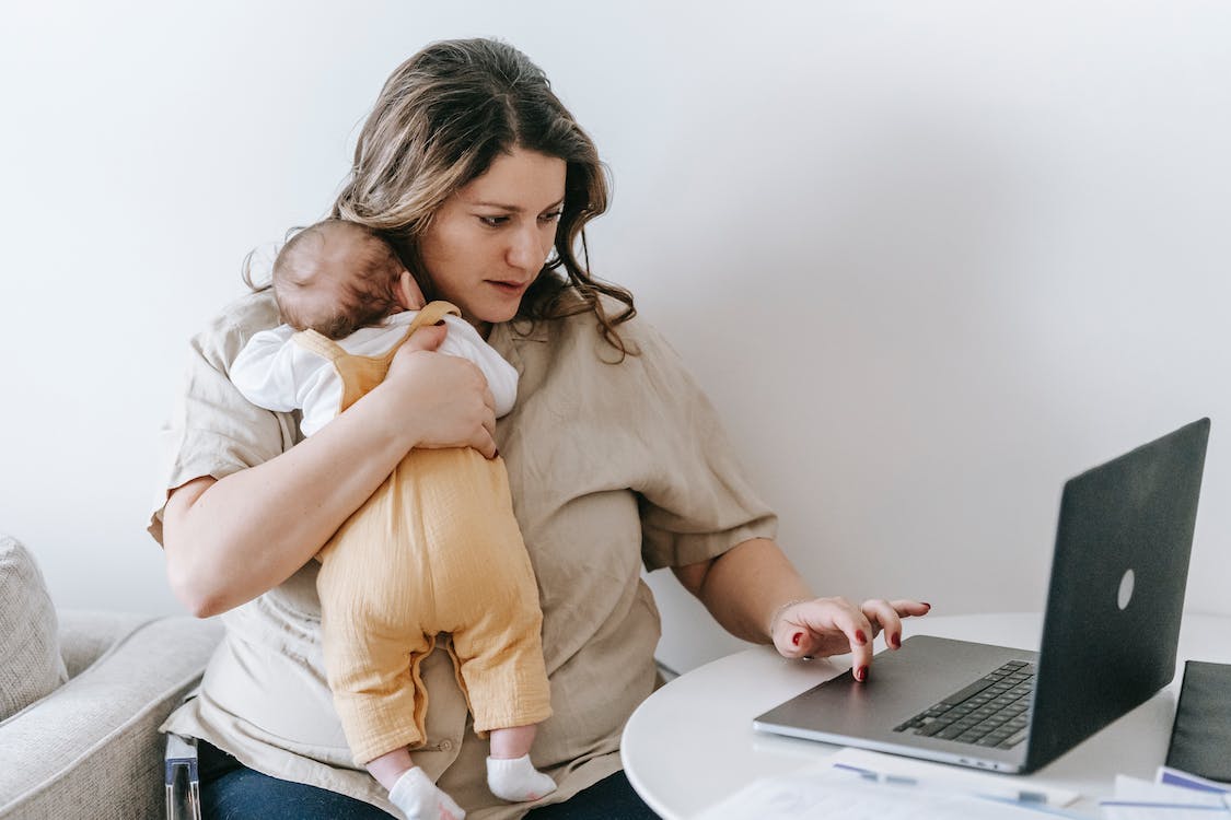 working mother cuddling a baby and typing in a laptop
